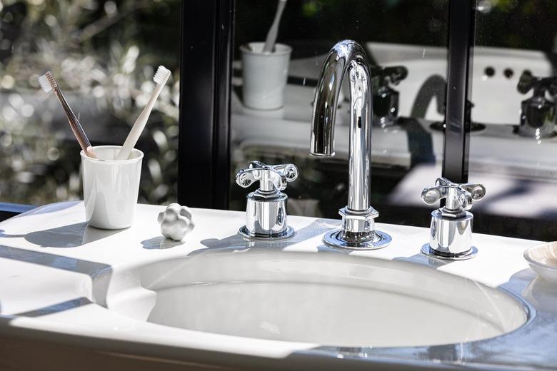 A sink faucet and countertop with a toothbrush cup in front of a window