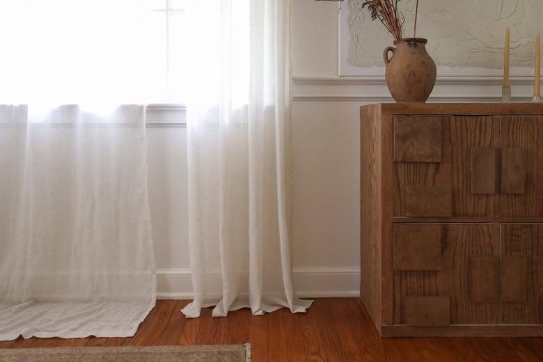 Linen curtains arranged to be measured, cut to floor length, modernist sideboard with traditional vase