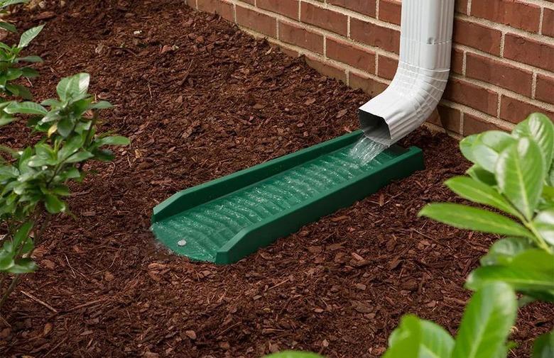 A green gutter splash block draining water from a gutter