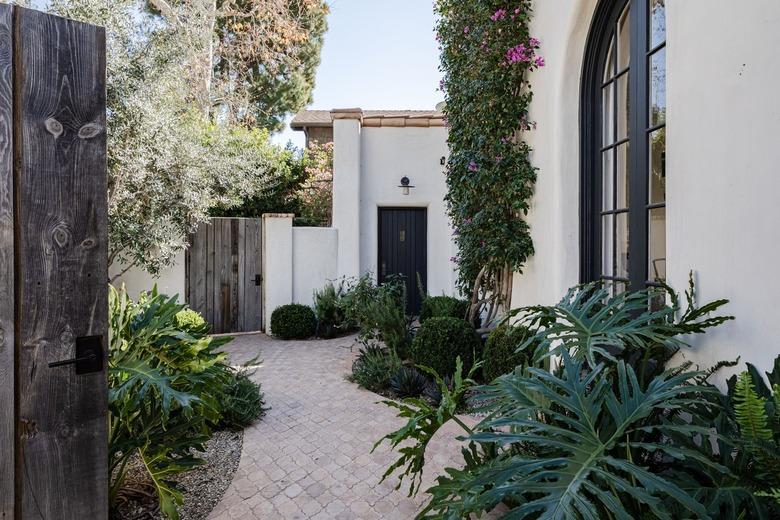 Side of a white home with large curved windows and tropical plants