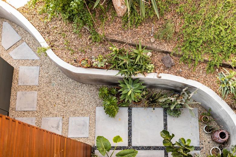 A curved white patio wall with plants and vases and a concrete path