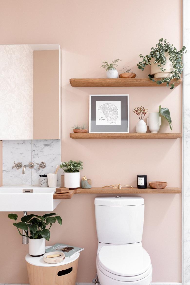 eco-friendly bathroom idea for pink bath with three wooden floating shelves above a toilet