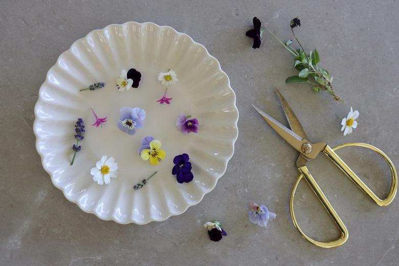 Assorted edible flowers on a white plate with gold scissors