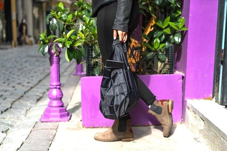 Person holding a black tote bag and walking down steps in front of a purple wall and planter