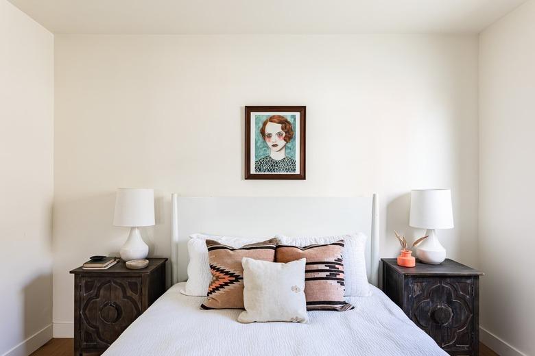 white bedroom with dark wood side tables and painting over bed