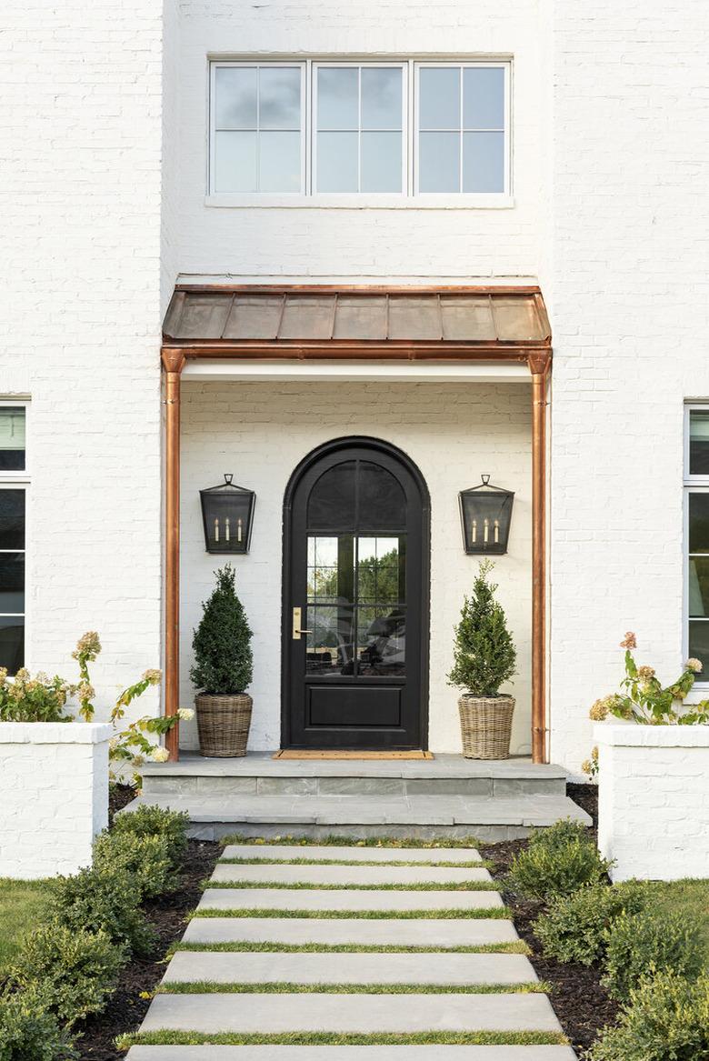 white brick farmhouse exterior with black door and copper details