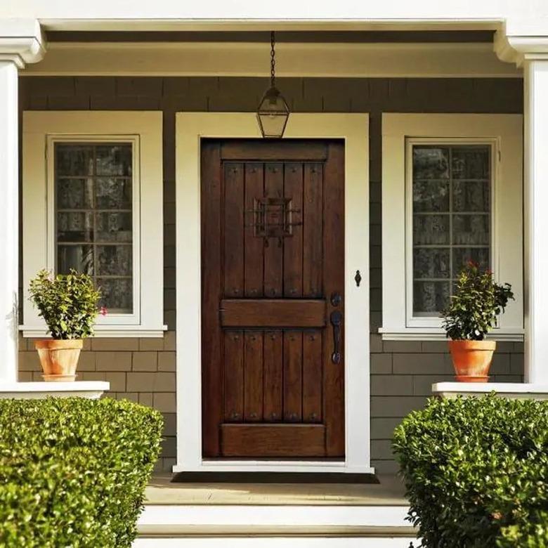 A rustic front door on a house with cedar shakes and two large windows