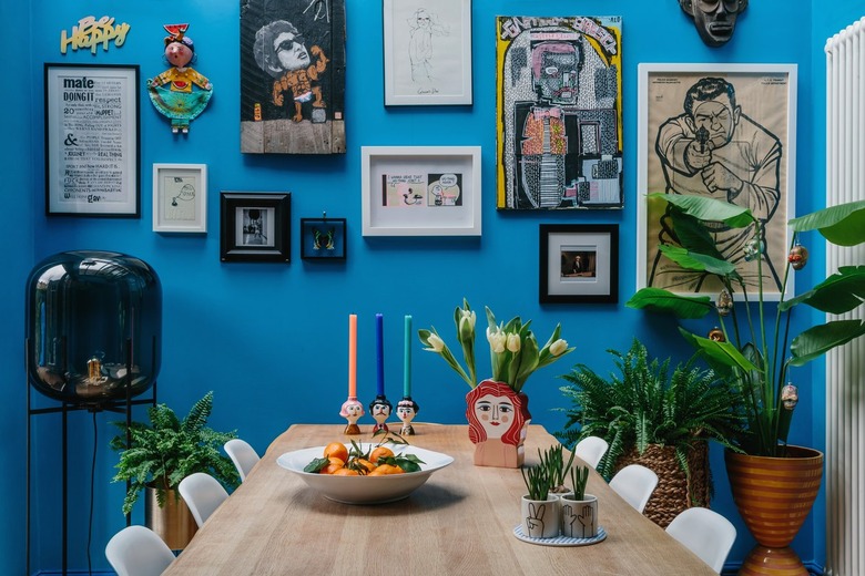 bright blue walls in a dining room with gallery wall art and white molded eames chairs at a wood dining table