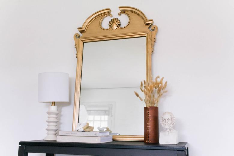 DIY gilded mirror on table with books, vase, lamp and bust