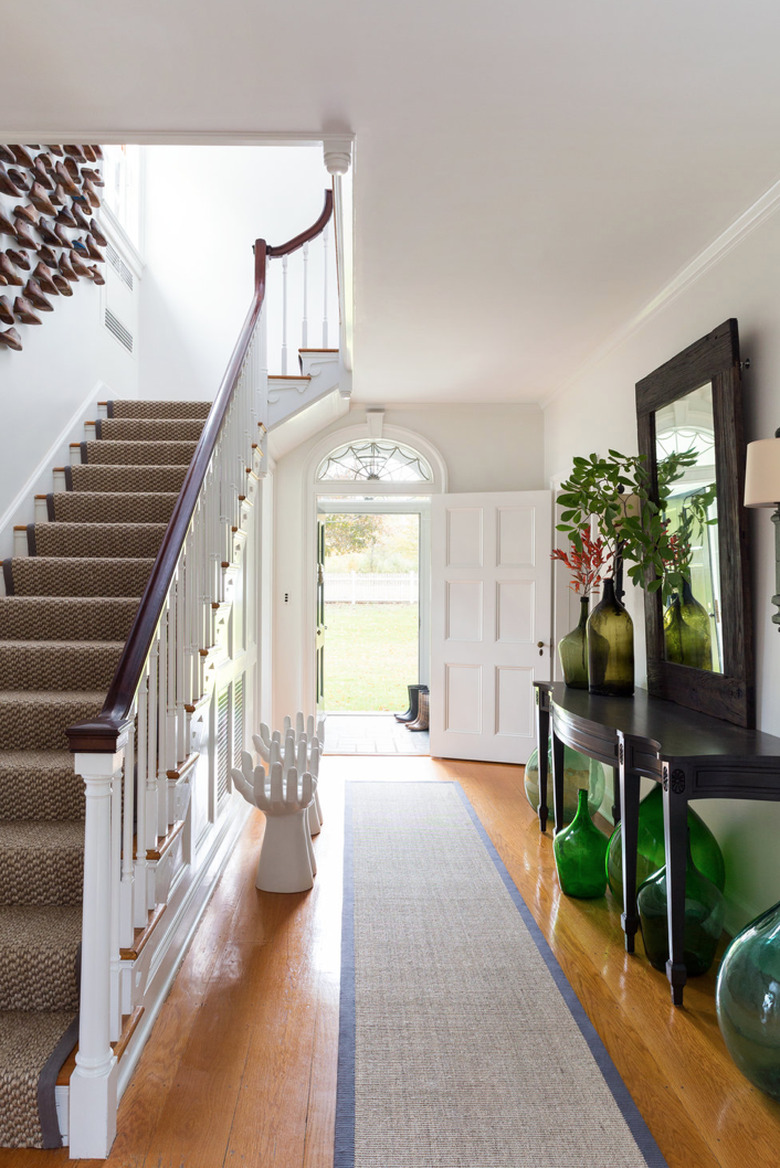 Hallway Runner Ideas in Entryway with jute runner, credenza, mirror, art, plants, stairs, front door.