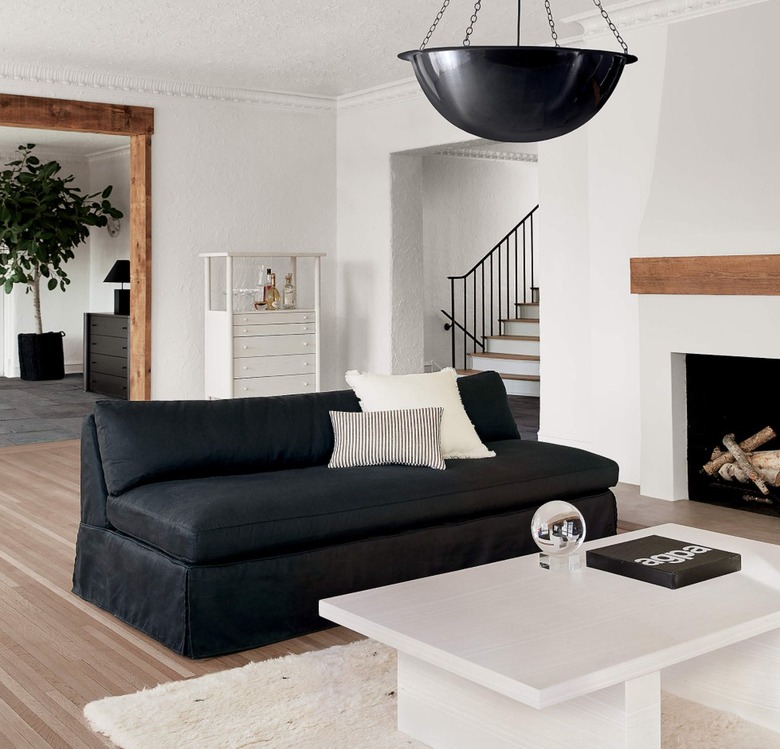 Living room with black slipcovered sofa, white coffee table, black pendant lamp, fireplace, rug.