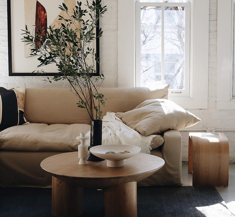 Living room with beige slipcovered sofa, coffee table, art, pillows, rug, end table.