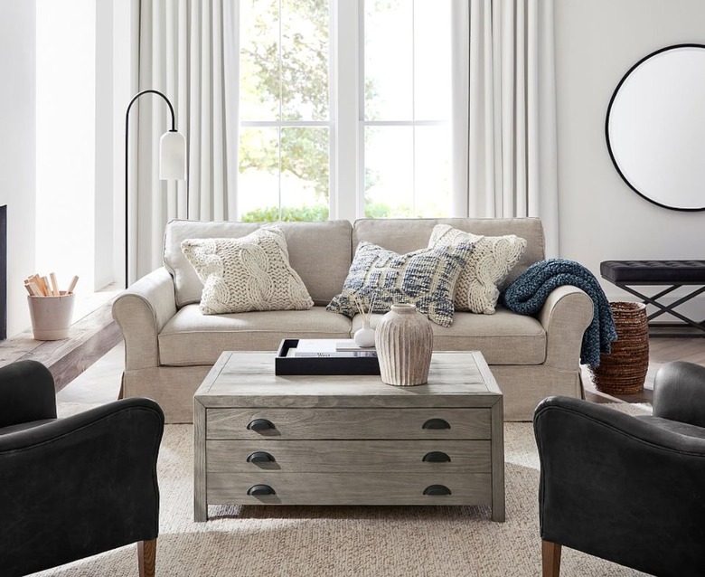 Living room with rolled arm slipcovered sofa, coffee table, leather wingback chairs, mirror, floor lamp, rug, pillows.