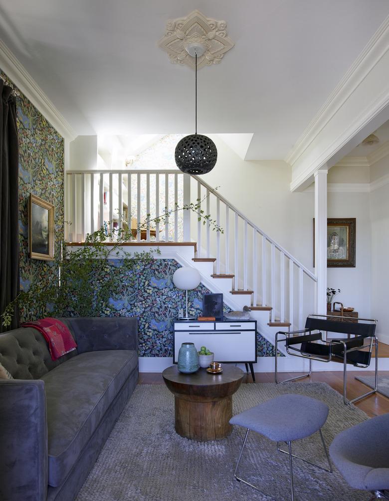 Living room with patterned wallpaper, velvet gray couch and vintage chairs