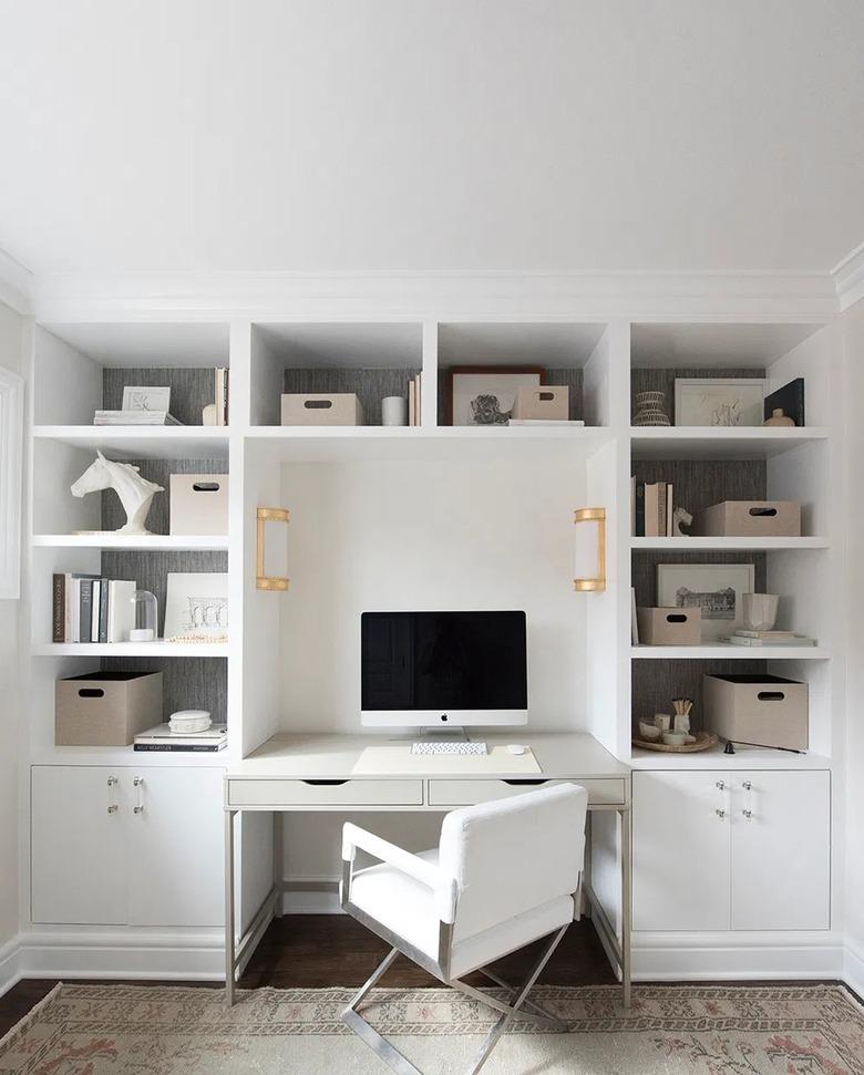 modern white home office with built-in shelving and brass sconces