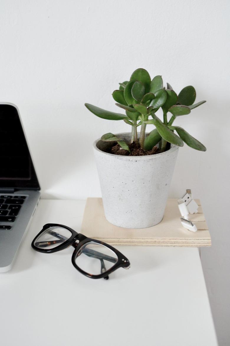 a cable organizer made out of a square of plywood with cables hanging from it and a potted plant inset