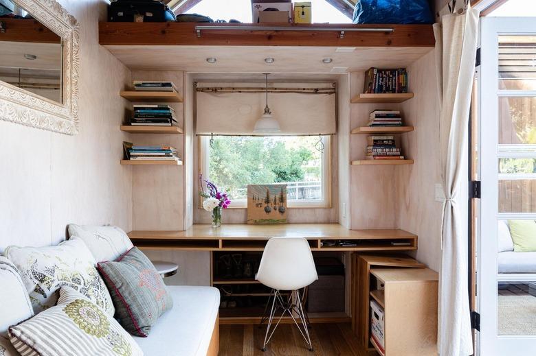 A small office space with a pendant light, canned lights above, and open shelving on both sides of the desk