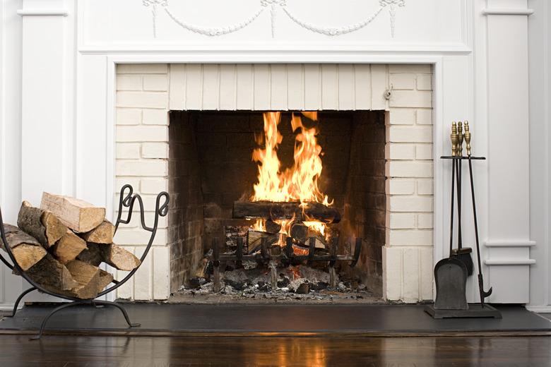 White brick fireplace with fire burning, stack of logs on rack, and fireplace tools