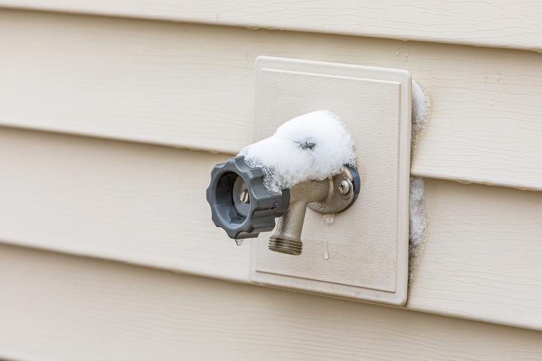 Outdoor water spigot covered in snow during winter. Home repair, maintenance and weatherproofing concept.