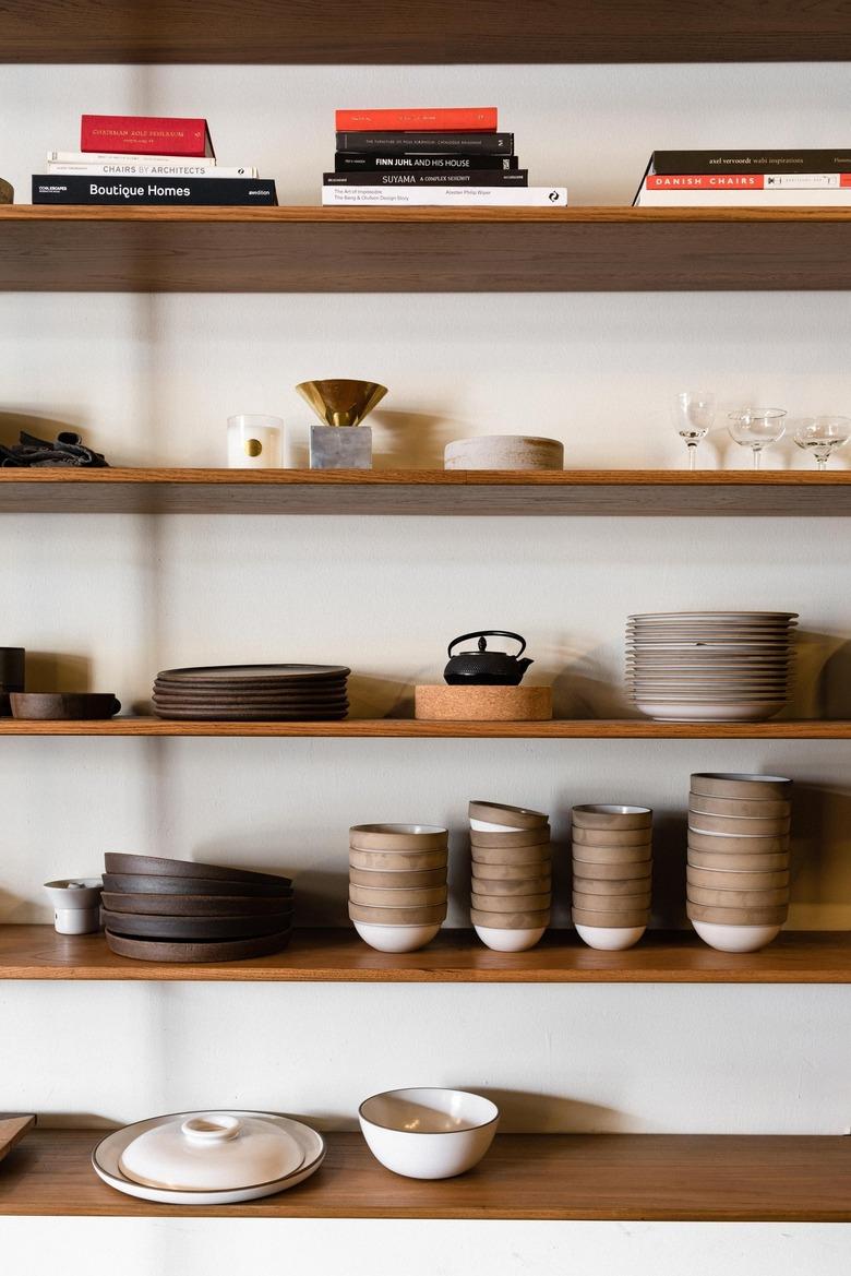 Wood shelves with books, brown and neutral dish ware, and a black teapot.