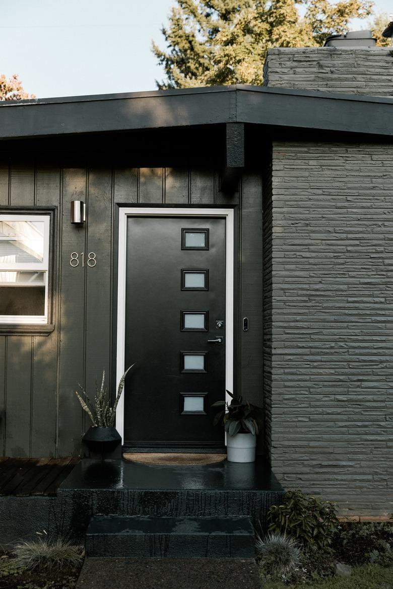 A gray and black mid-century house with a brick chimney