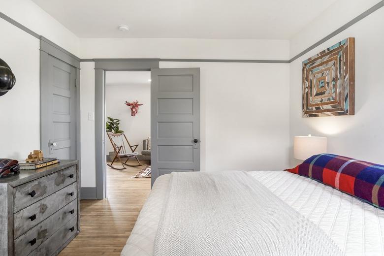 Minimalist bedroom with wood floors, gray dresser, bedding and doors