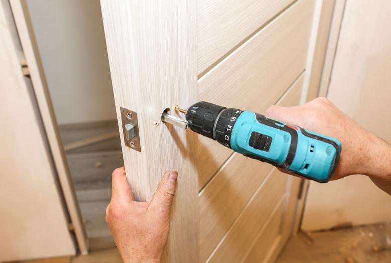 Man is installing the doors handle with a drill. Repair works. Maintenance in the apartment.