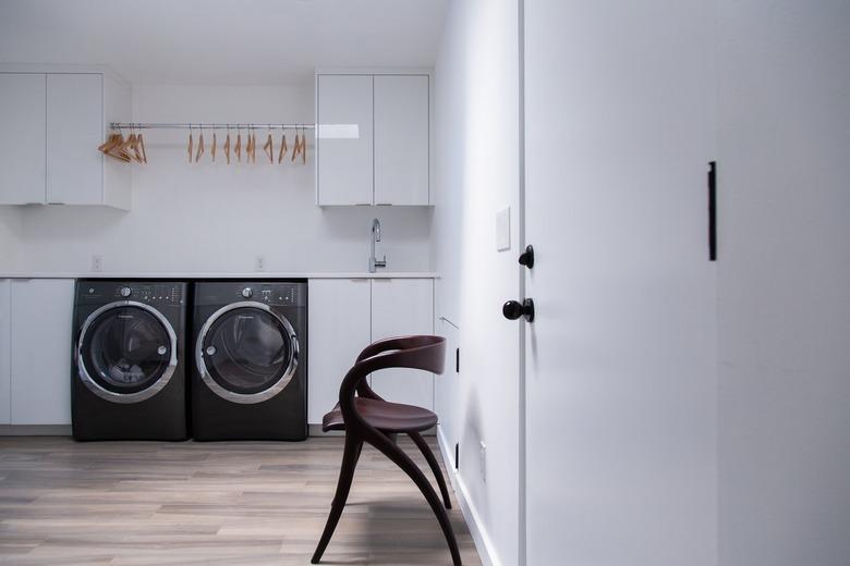 Modernist wood chair in a Minimalist laundry room with white cabinets, and a black washer and dryer.