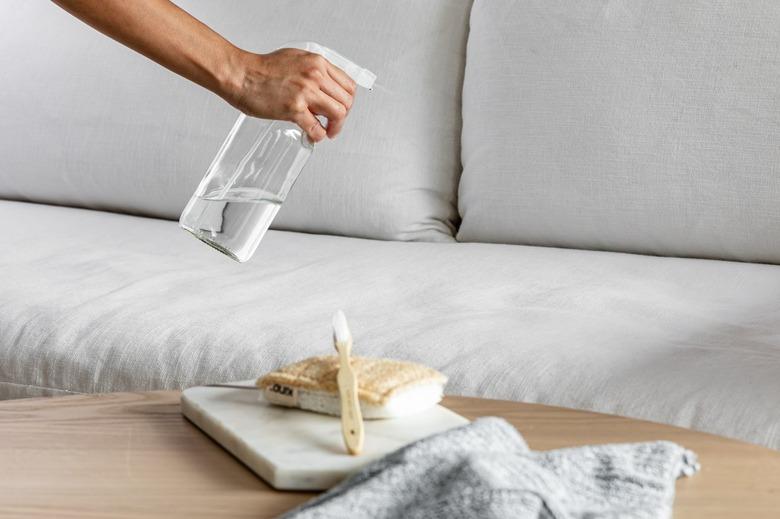 A person spraying a sofa with cleaning solution.