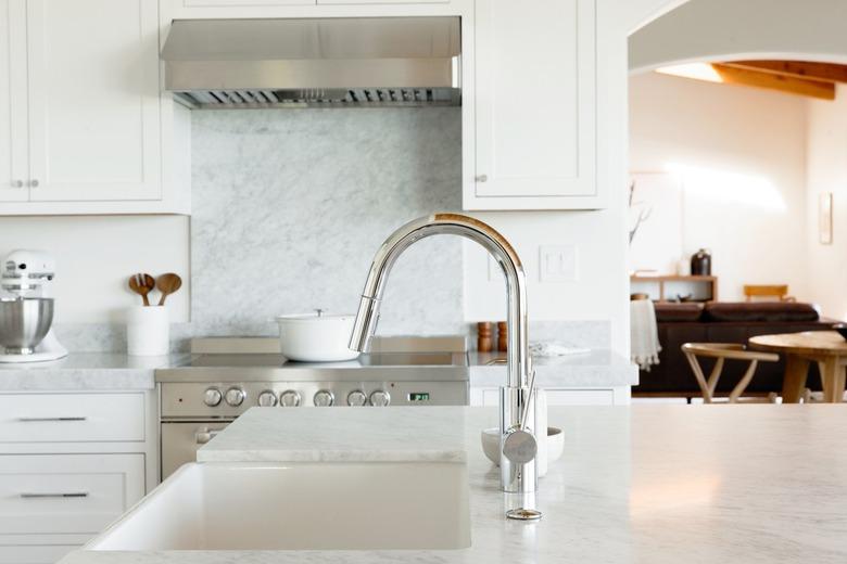 Kitchen sink in a marble countertop with a chrome faucet. Behind it, a stainless steel range with a white dutch oven on the stovetop.