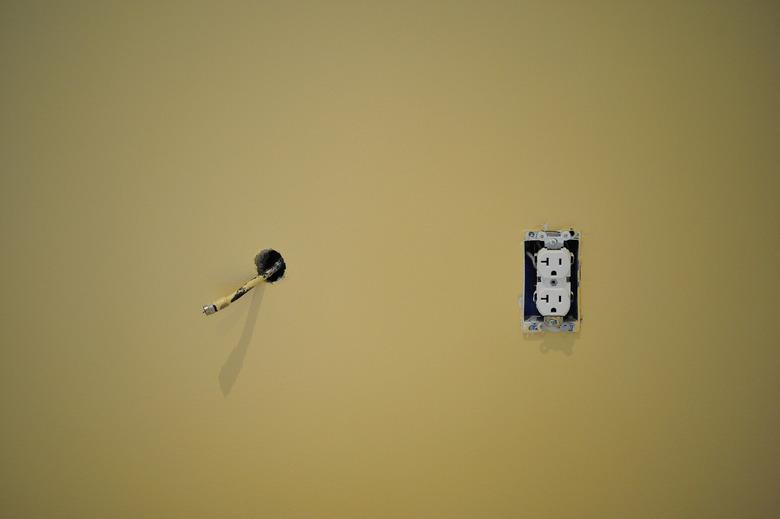 Coaxial cable hanging out of freshly painted wall next to an electric outlet 3 prong plug during renovation and construction