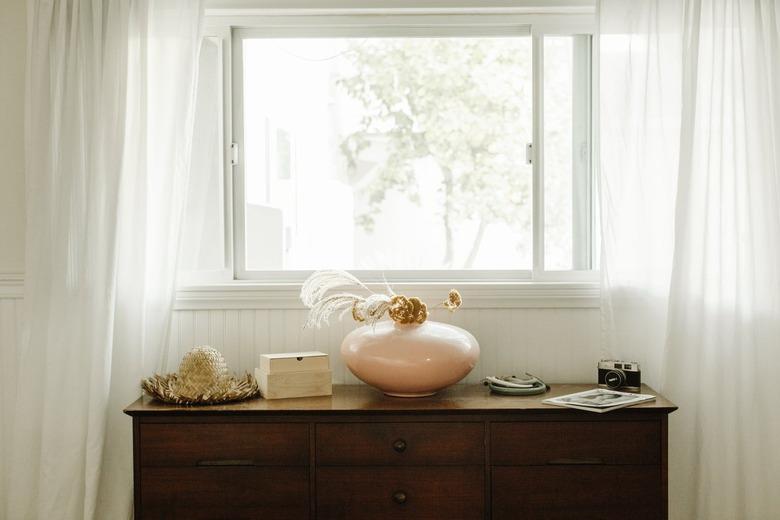 Open window with white flowing curtains, a dark wood credenza below with neutral decor