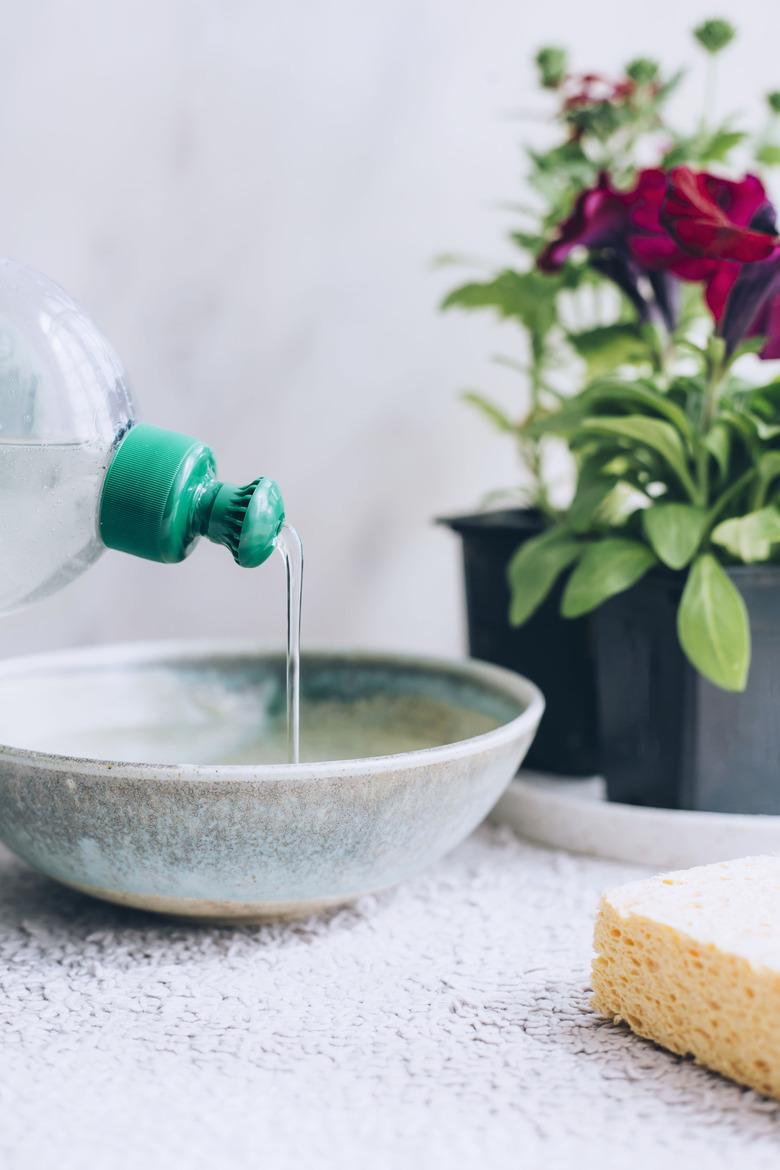 dish soap being poured into ceramic bowl with sponge