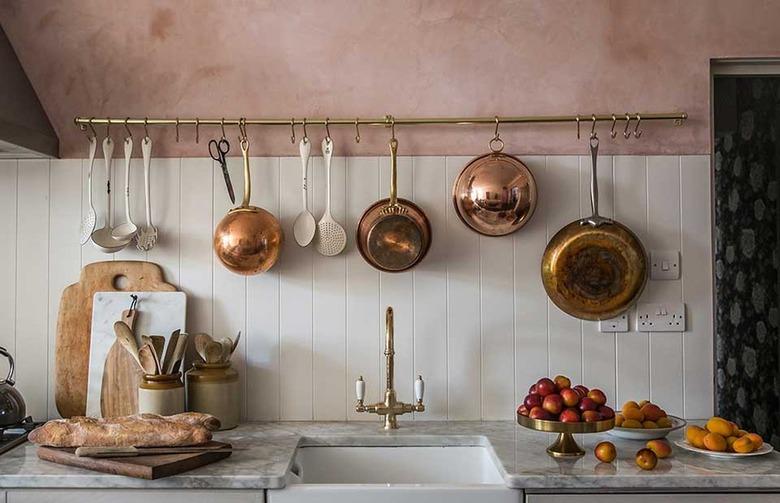 pink kitchen with copper pots hanging from brass utensil rack