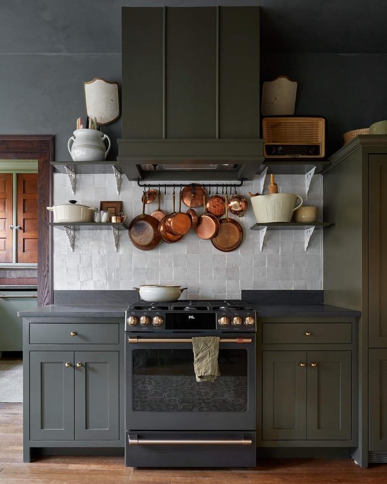 Dark kitchen with green cabinets and hanging copper pots.