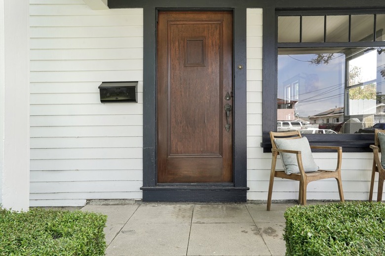 A solid wood front door on a white house with a chair on the front porch