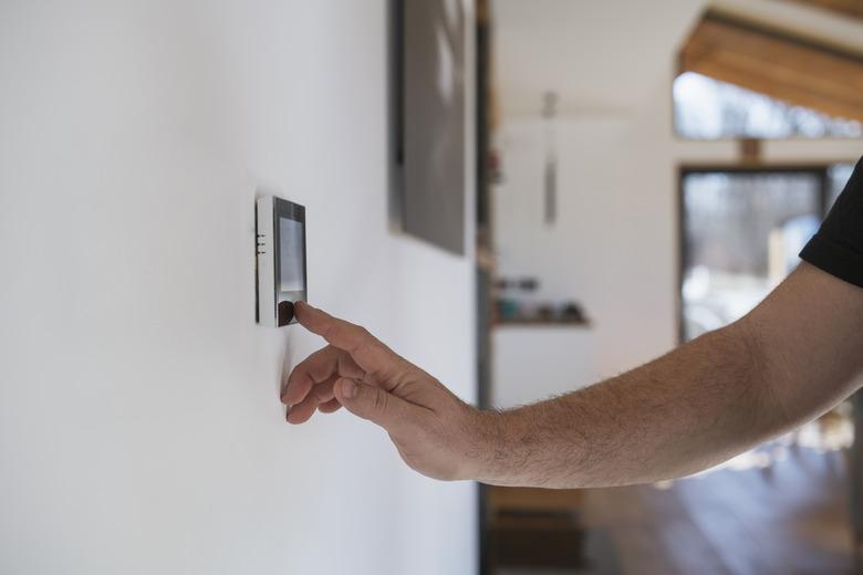 Man at home adjusting thermostat with device on the wall.