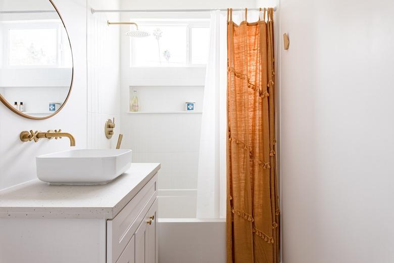 A minimalist white-walled bathroom with a white vanity and gold-orange accents.