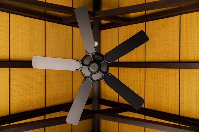 brown indoor ceiling fan on an exposed wooden support beam, with a decorate wooden ceiling, in the hall of living room of a contemporary home interior,home interior design concept