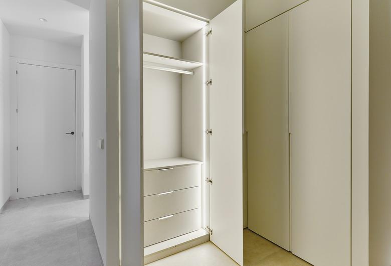 Opened door of lighted white wooden built-in wardrobe.