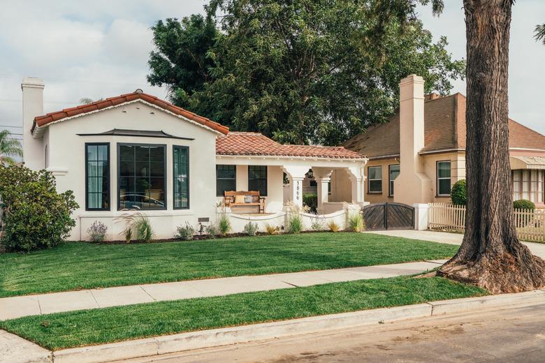 Spanish-style home with large tree in the front and green grass