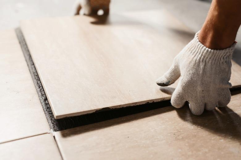 The hands of the tiler are laying the ceramic tile on the floor. Close up macro shot. Home renovation and building new house concept