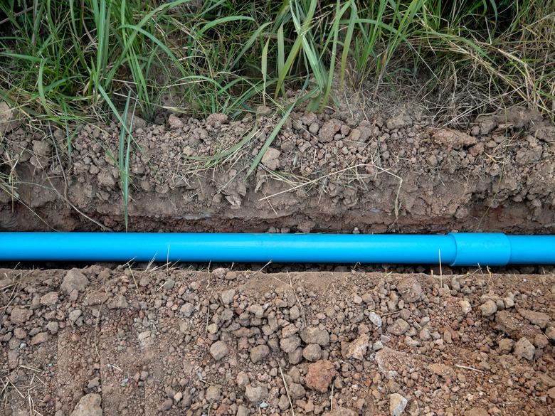 Small PVC pipe lying in a trench near pavement for water supply system.