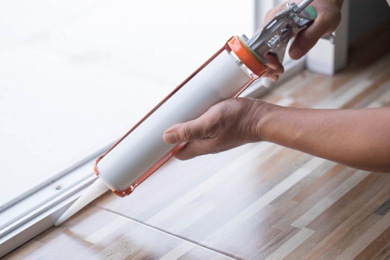 Men's hand uses silicone adhesive with a glue gun to repair worn windows.