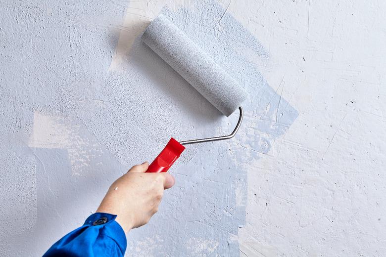 Home painter is painting walls with paint roller and paints during renovation.