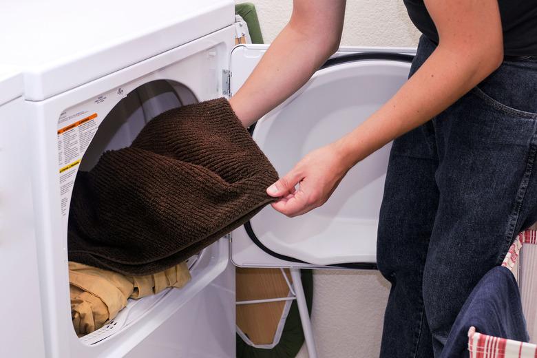 A woman inserting a brown towel into the dryer with a set of sheets