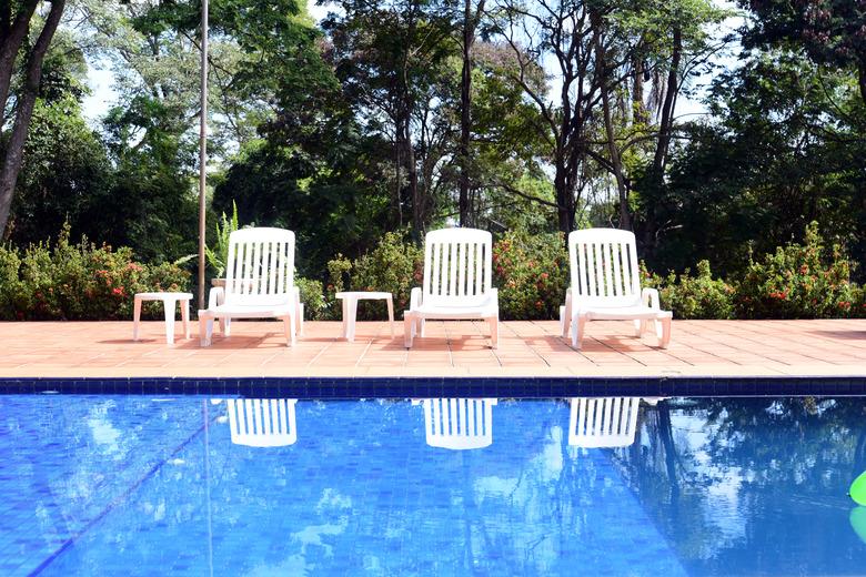 Pool with white chairs and a garden in the background.