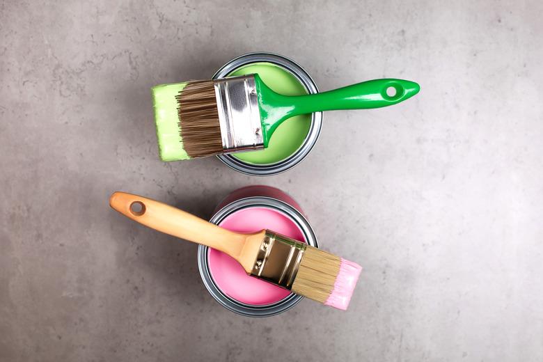 Paintbrushes on cans of green and pink paint.