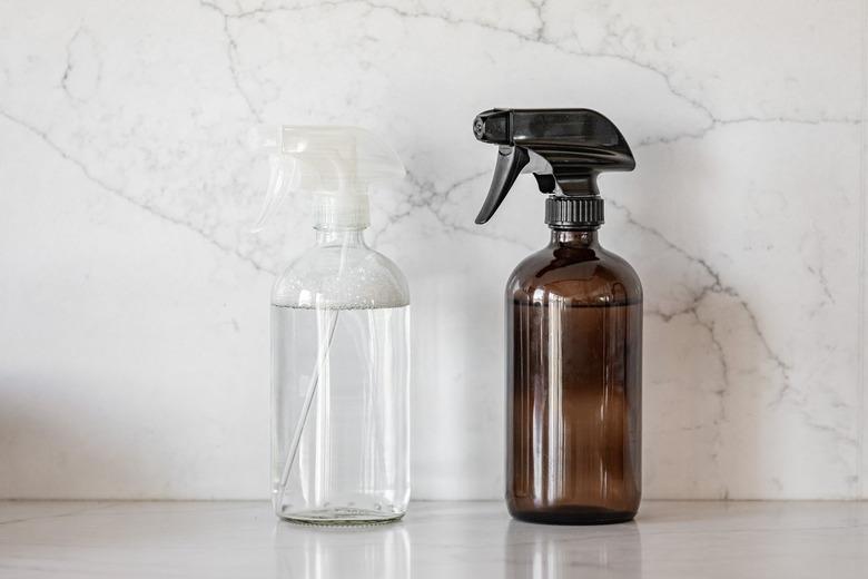 Two unmarked spray bottles, one clear and one amber-colored, sitting on a countertop with a marble backsplash