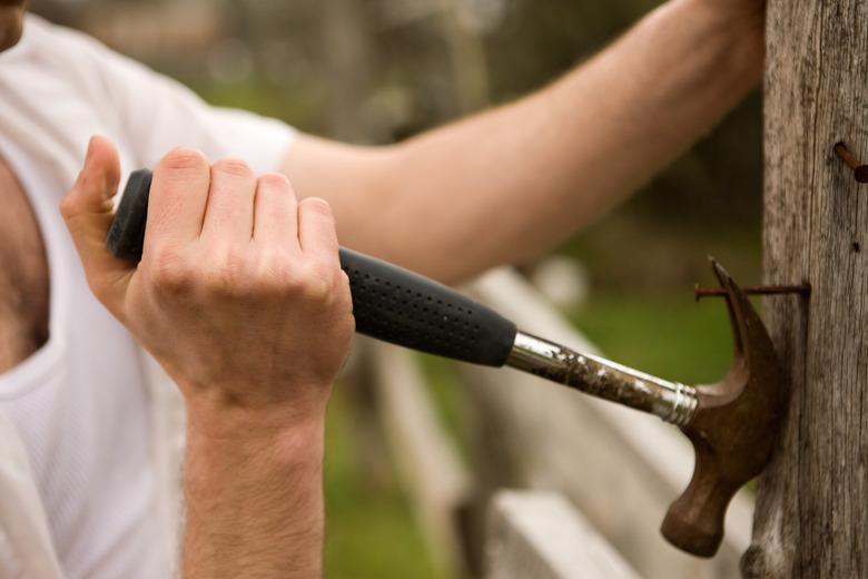 Farmer pulling nail from fencepost with hammer.